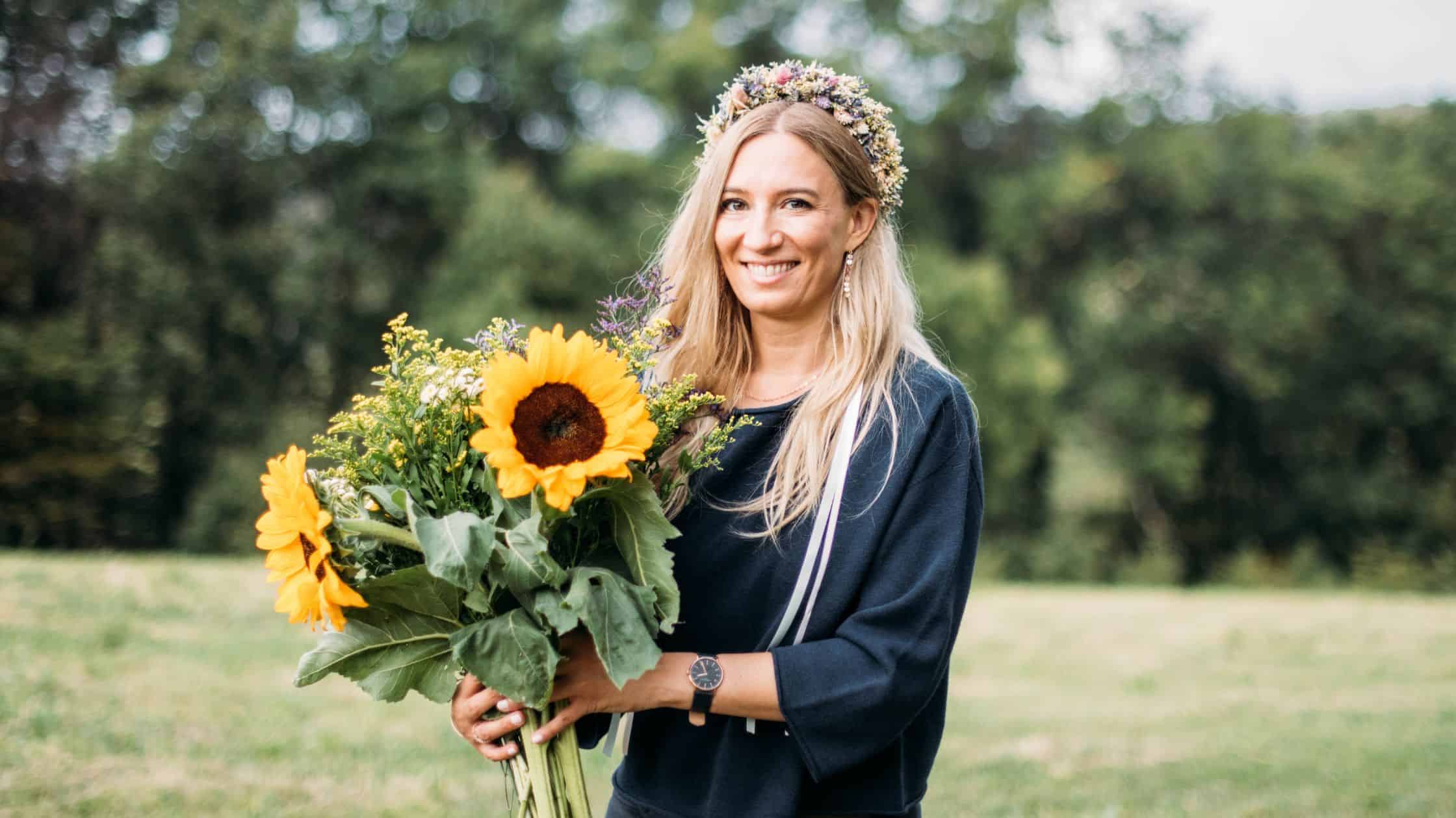 Frau mit Blumenkranz und Sonnenblumenstrauß auf einer Wiese