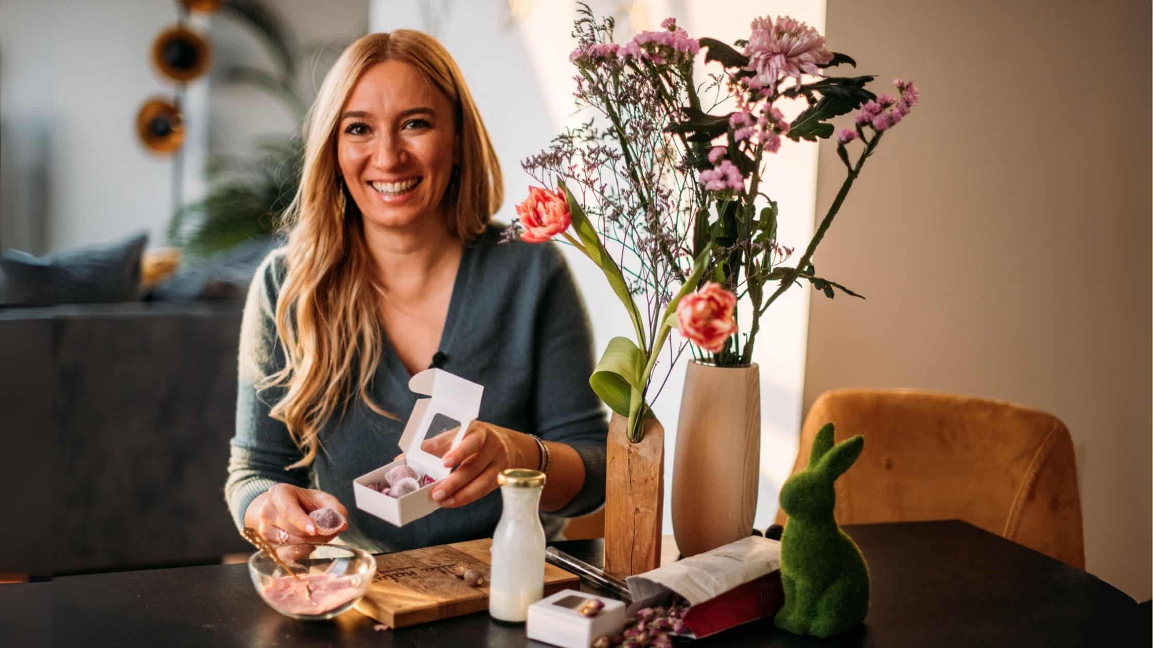 Lächelnde Frau mit selbstgemachten Rosenpralinen und frischen Blumen am Tisch